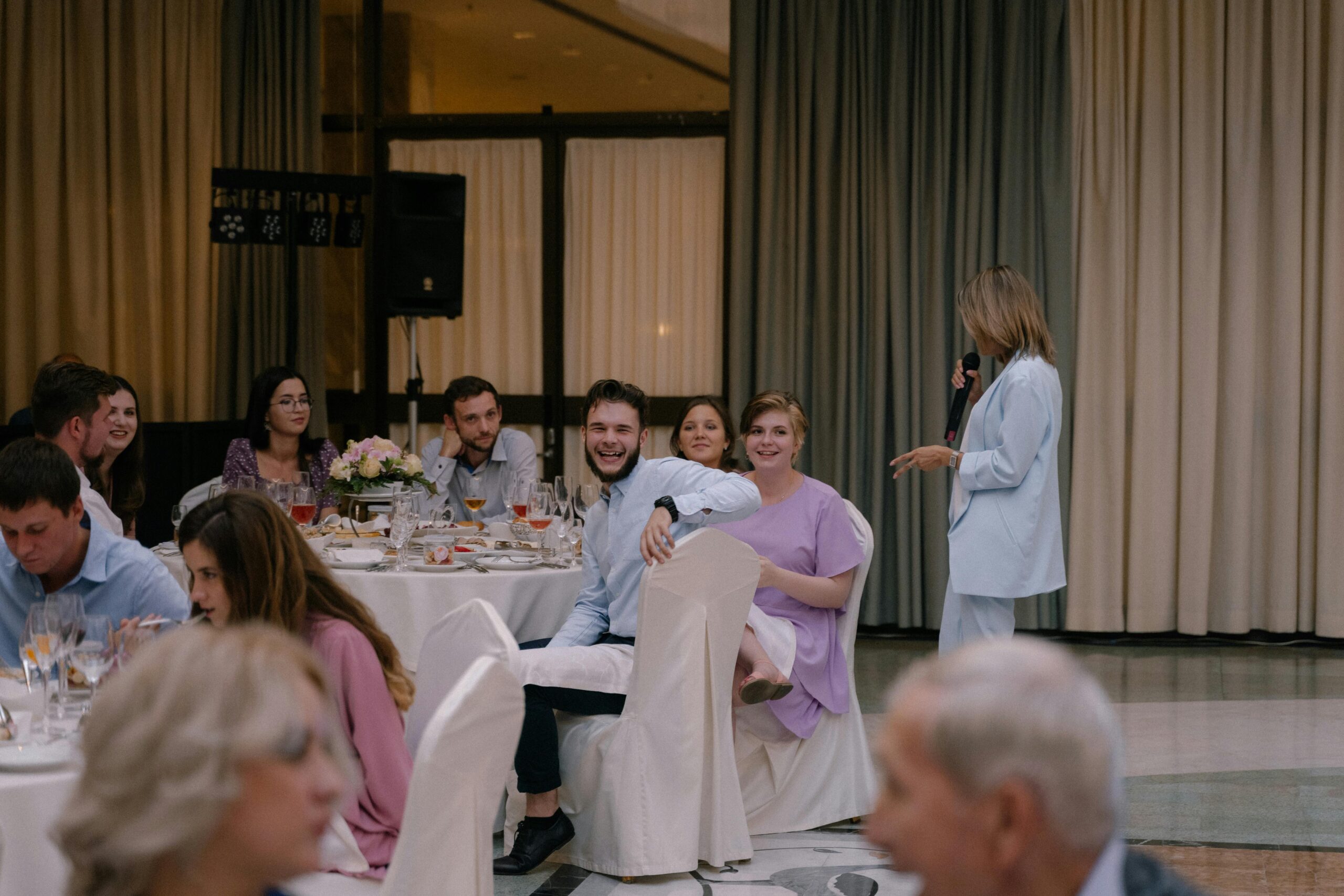 A women delivers a heartfelt speech at a wedding reception, entertaining family and guests during the indoor celebration.