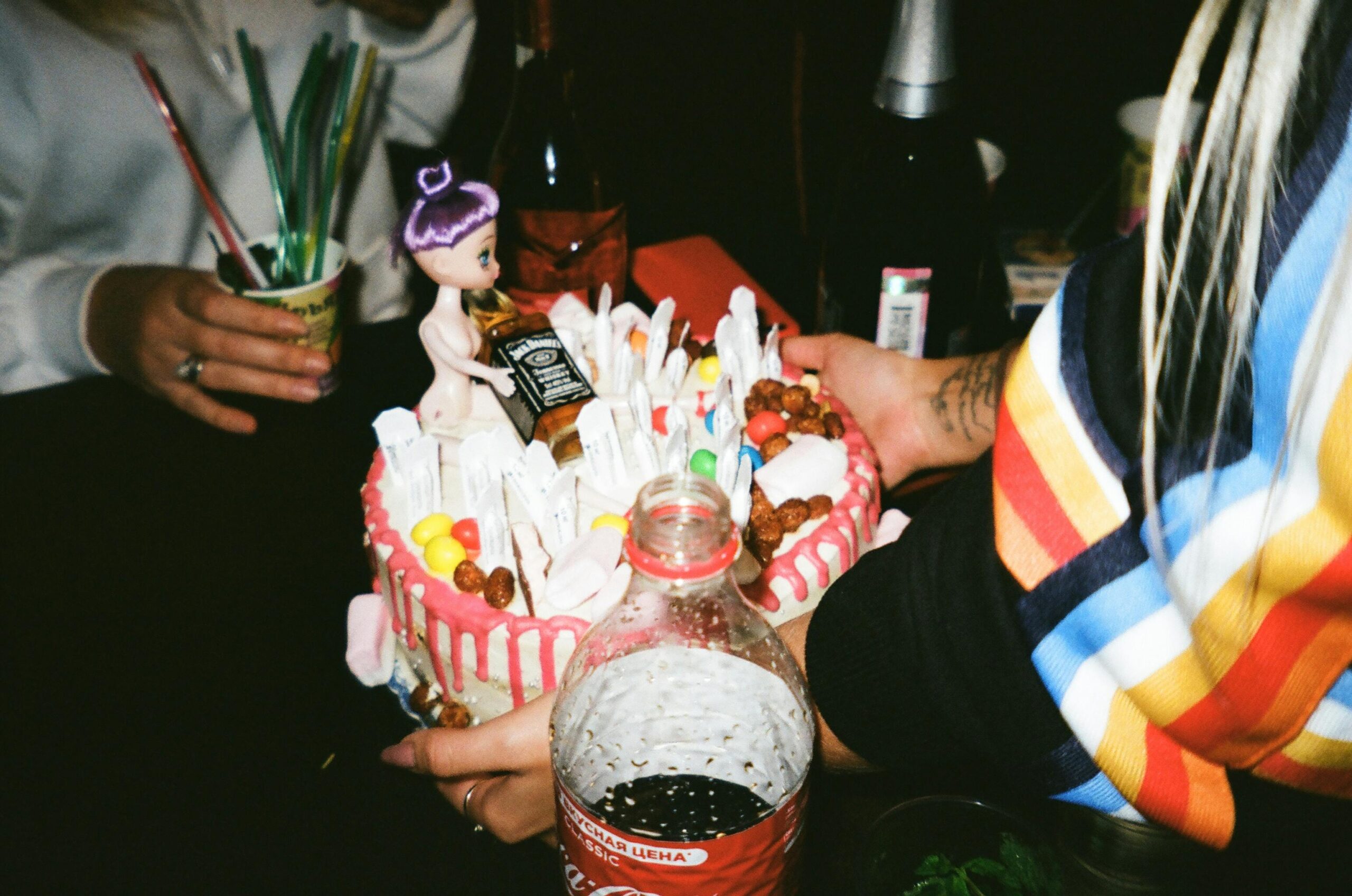 A person presents a cake alongside a bottle of soda, symbolizing a joyful birthday celebration.