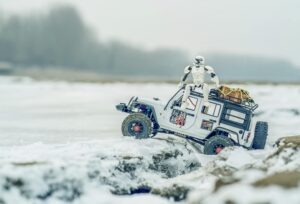 A toy jeep is stationed next to a snowy field, embodying fun and exploration in a chilly outdoor setting.