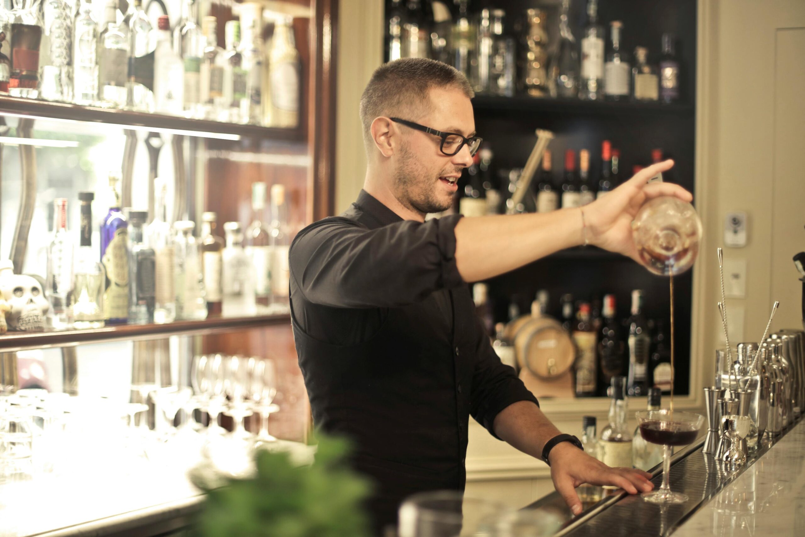 A man stands behind the bar, expertly crafting a drink, highlighting professionalism in the alcohol service industry.