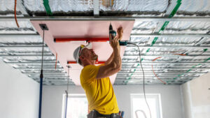 A skilled technician wearing safety gear, carefully installing a modern ceiling panel using advanced tools, in a well-lit interior space.