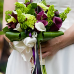 A bride elegantly holds a bouquet of green and purple flowers, showcasing the artistry of a Calgary wedding florist.