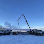 Concrete pumping at a snowy construction site with boom pump and mixer trucks working at dawn in Alaska.