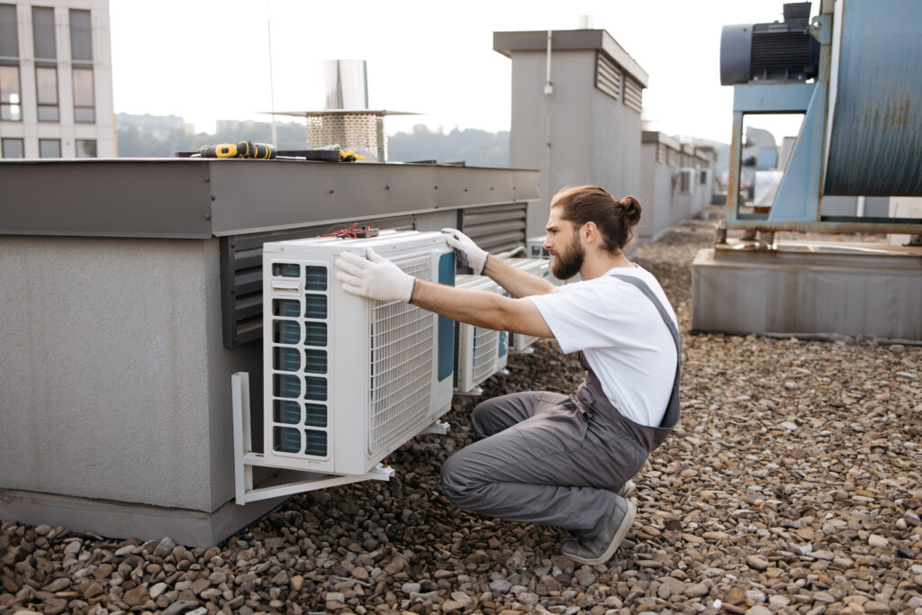adult-bearded-construction-worker-crouching-keeping-hands-air-conditioner-while-checking-serviceability-caucasian-qualified-man-wearing-gloves-examining-device-roof-factory-1024x683 Professional Air Conditioning Installation in Clifton, NJ – Get a Free Quote