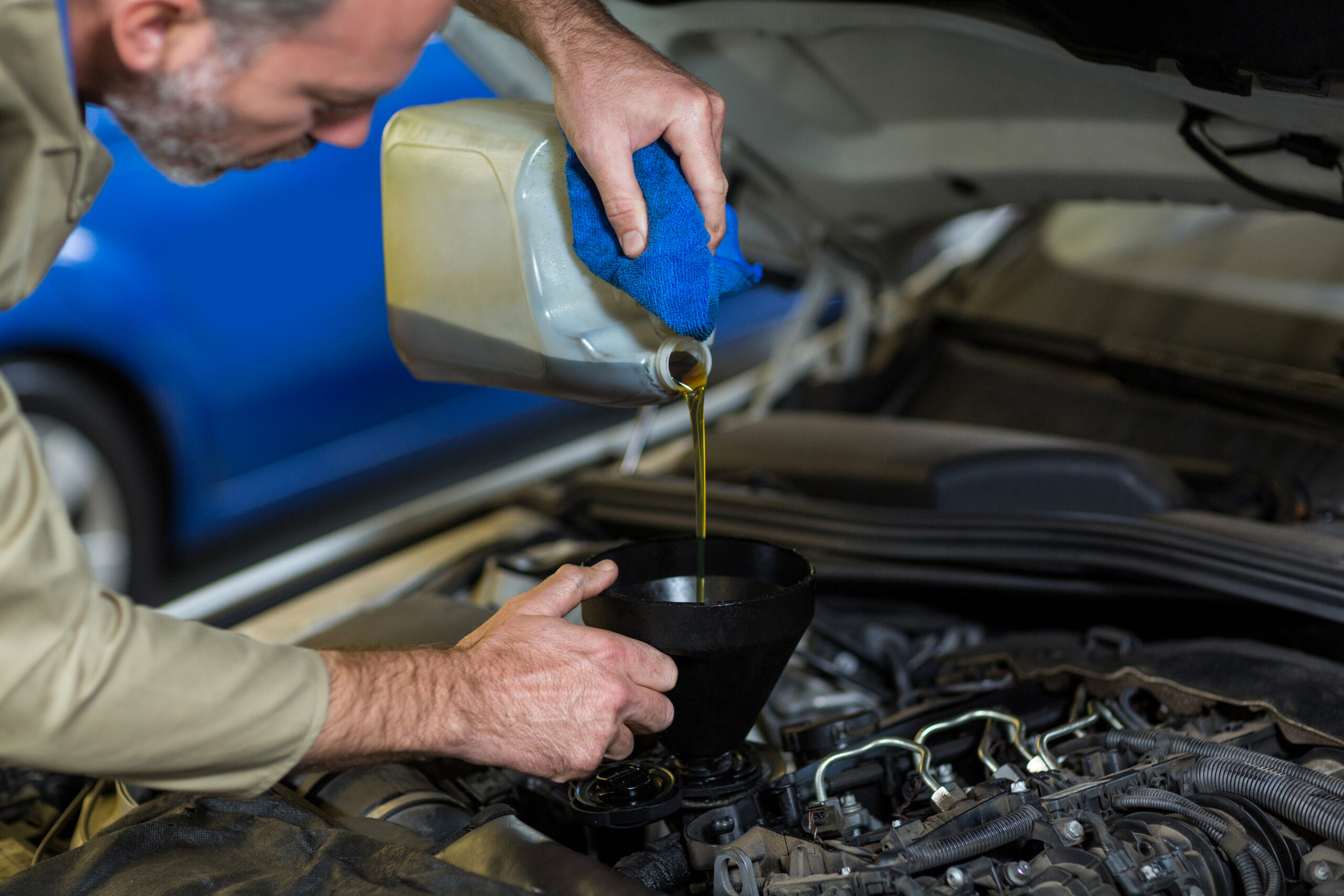A mechanic pouring fresh engine oil into a car engine, emphasizing the importance of regular oil change service for better fuel efficiency.